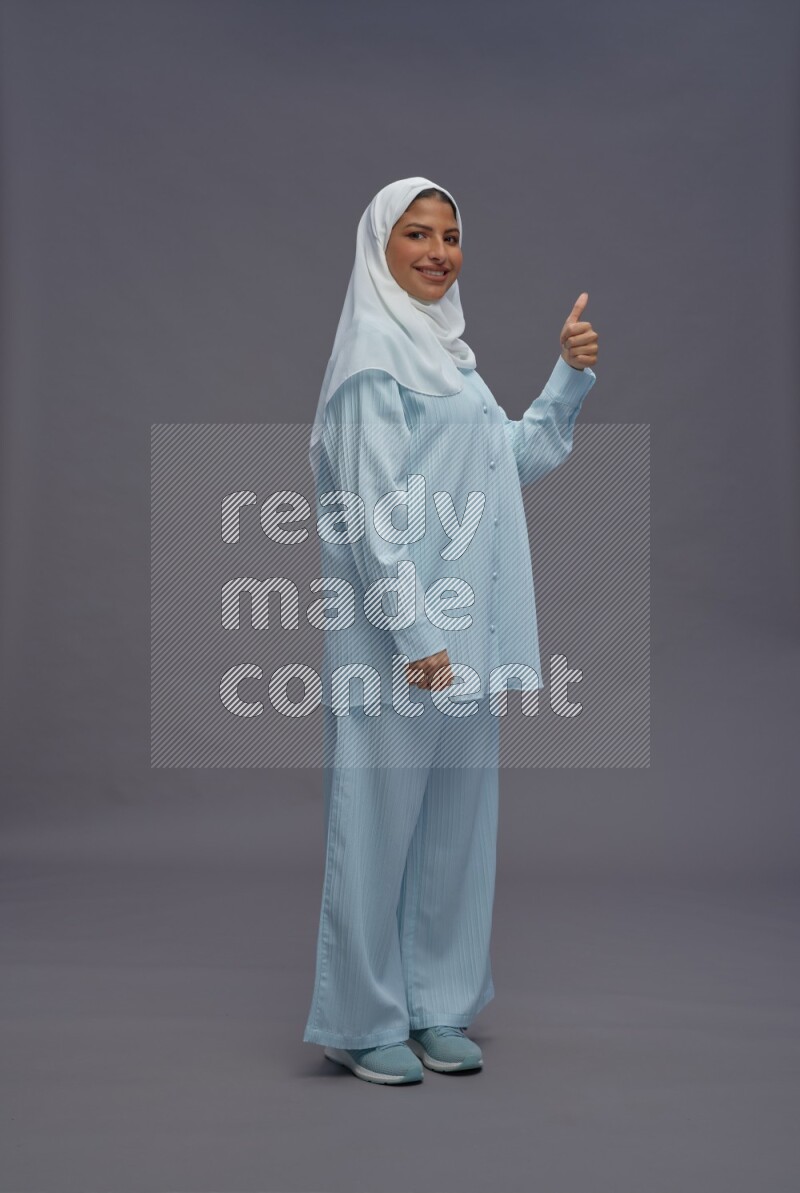 Saudi woman wearing hijab clothes standing interacting with the camera on gray background