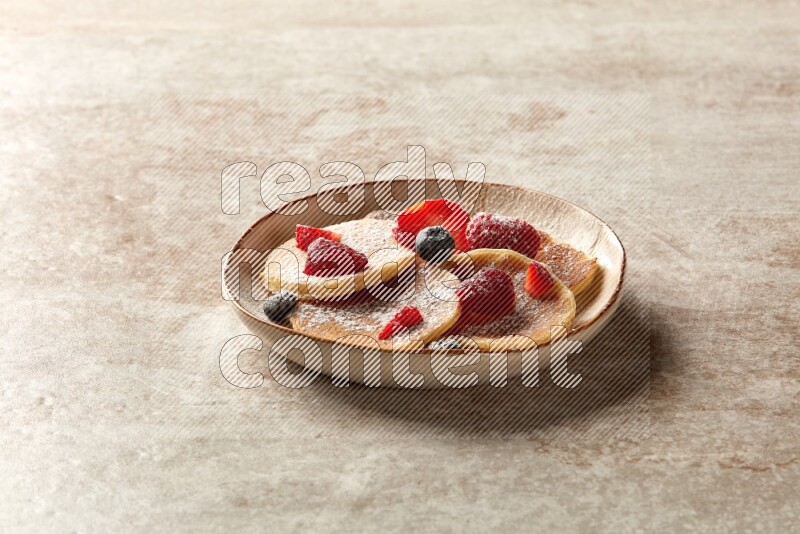 Five stacked mixed berries mini pancakes in an irregular plate on beige background