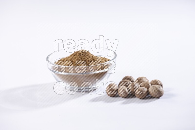 A glass bowl full nutmeg powder with the whole seeds beside it on a white flooring