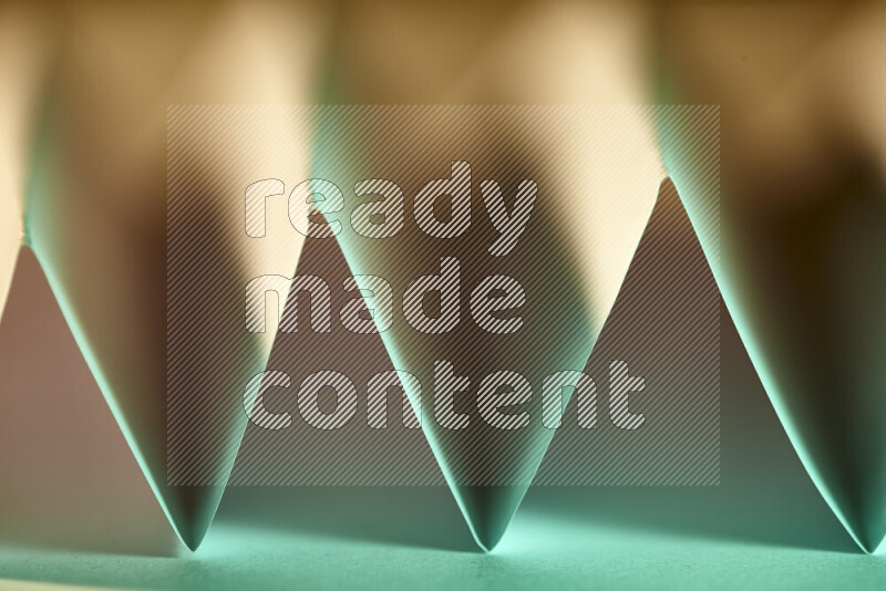 A close-up abstract image showing sharp geometric paper folds in green gradients and warm tones