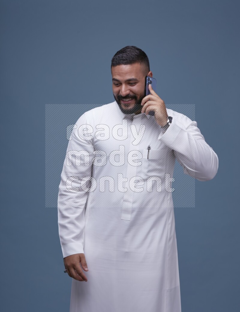 A Saudi man calling on blue background wearing Saudi Thob