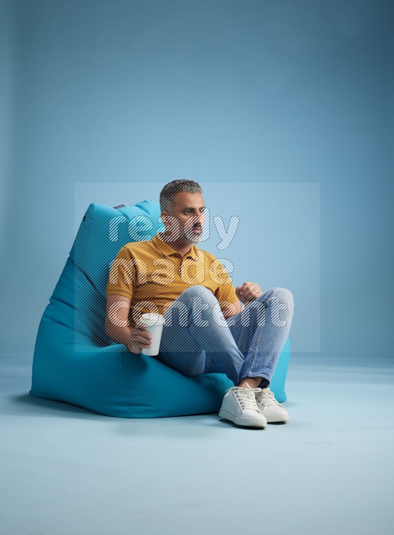 A man sitting on a blue beanbag and drinking coffee