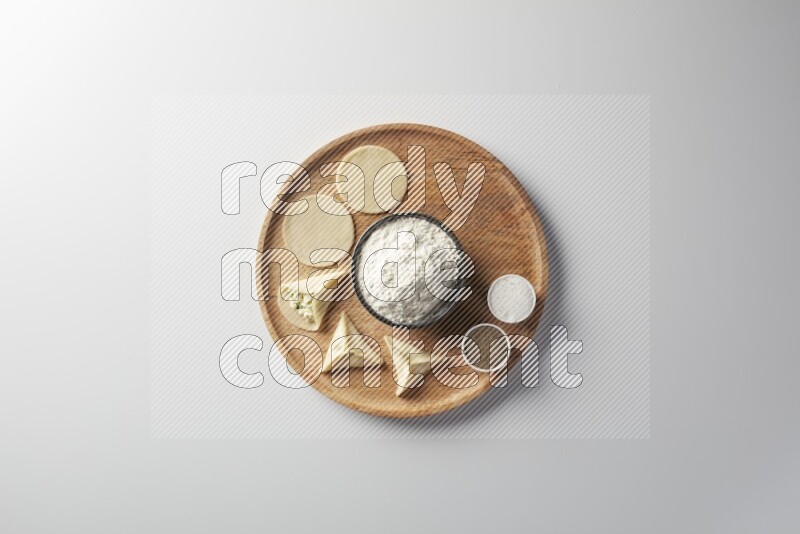 two closed sambosas and one open sambosa filled with cheese while flour, salt, and black pepper aside in a wooden dish on a white background