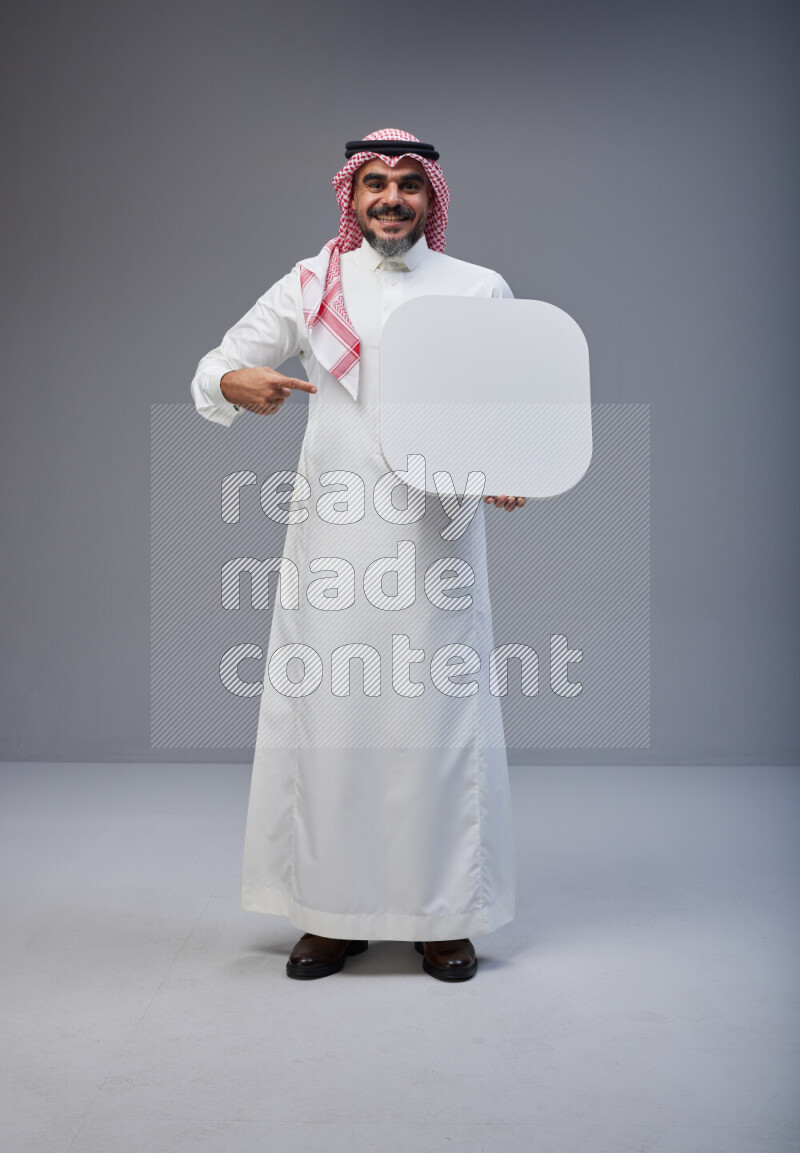 Saudi man Wearing Thob and red Shomag standing holding social media sign on Gray background