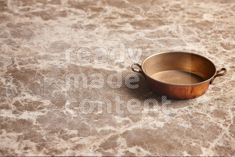 A small copper pan on beige marble background