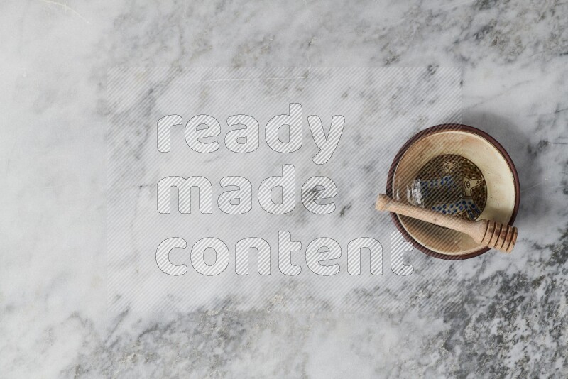 Decorative pottery plate with wooden honey dipper in it on grey marble background