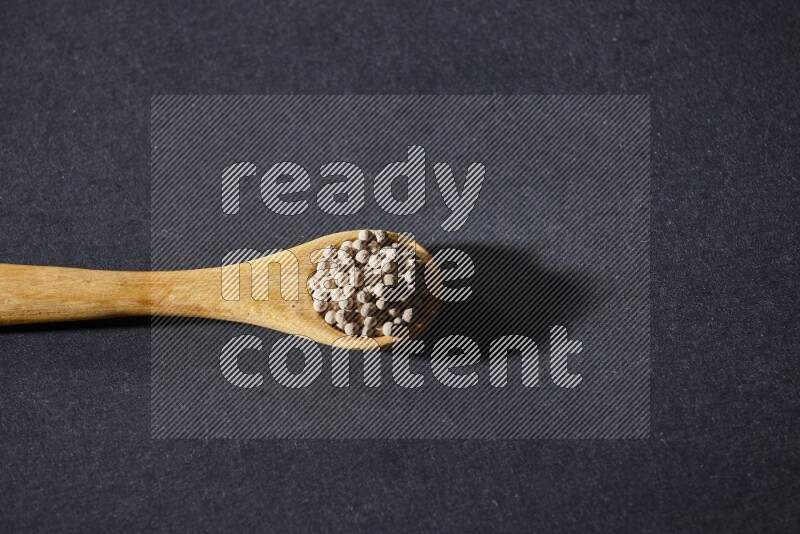 A wooden spoon full of white pepper beads on black flooring