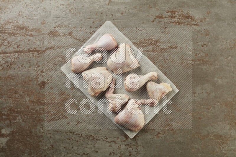 Mixed fresh chicken pieces on a parchment paper direct on a textured rustic background