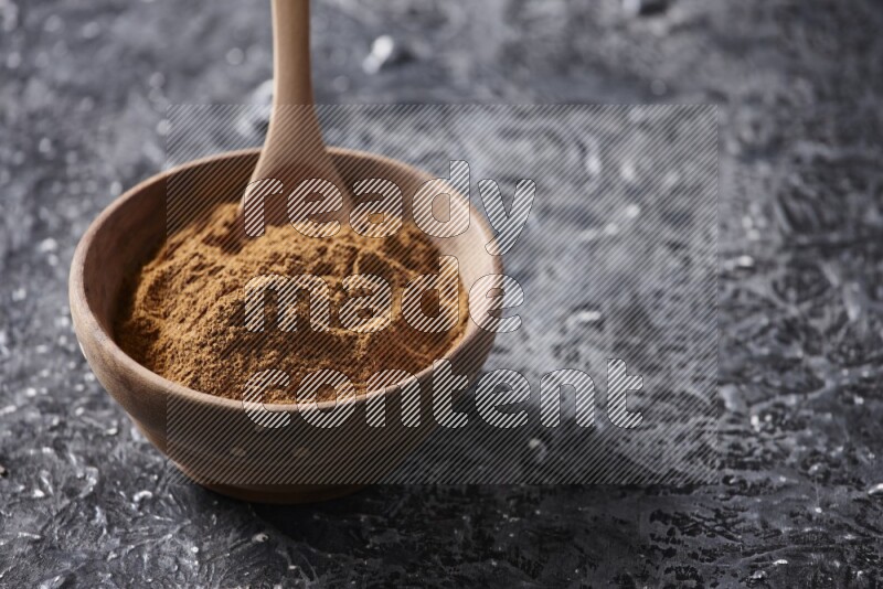 Wooden bowl full of cinnamon powder with a wooden spoon on a textured black background in different angles