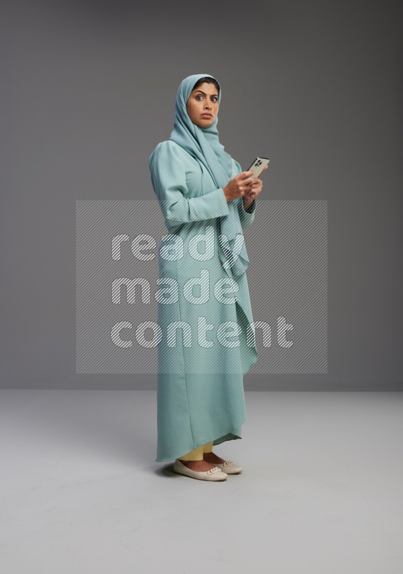 Saudi Woman wearing Abaya standing texting on phone on Gray background