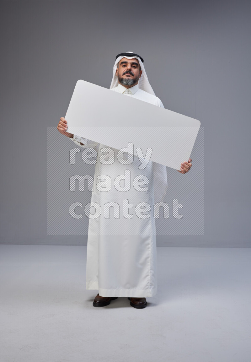 Saudi man Wearing Thob and white Shomag standing holding board on Gray background