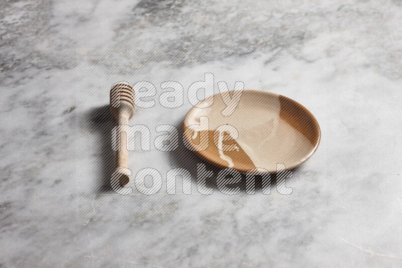 Multicolored pottery plate with wooden honey dipper on the side on grey marble background