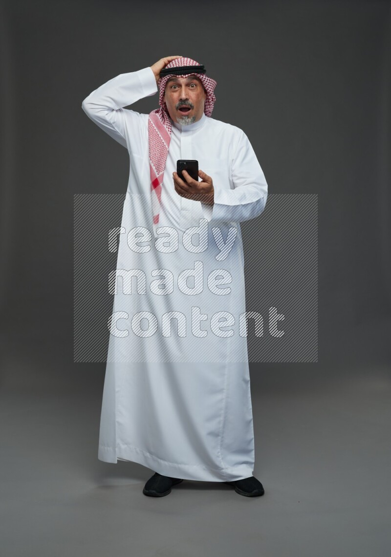 Saudi man with shomag Standing texting on phone on gray background