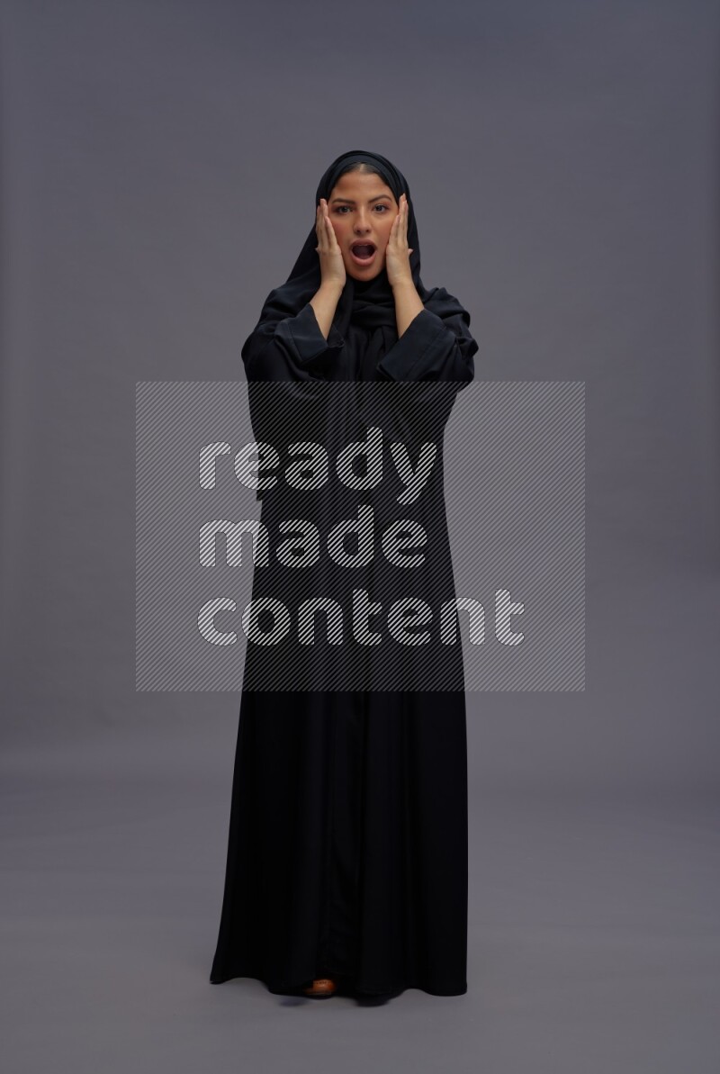 Saudi woman wearing Abaya standing hands behind head on gray background