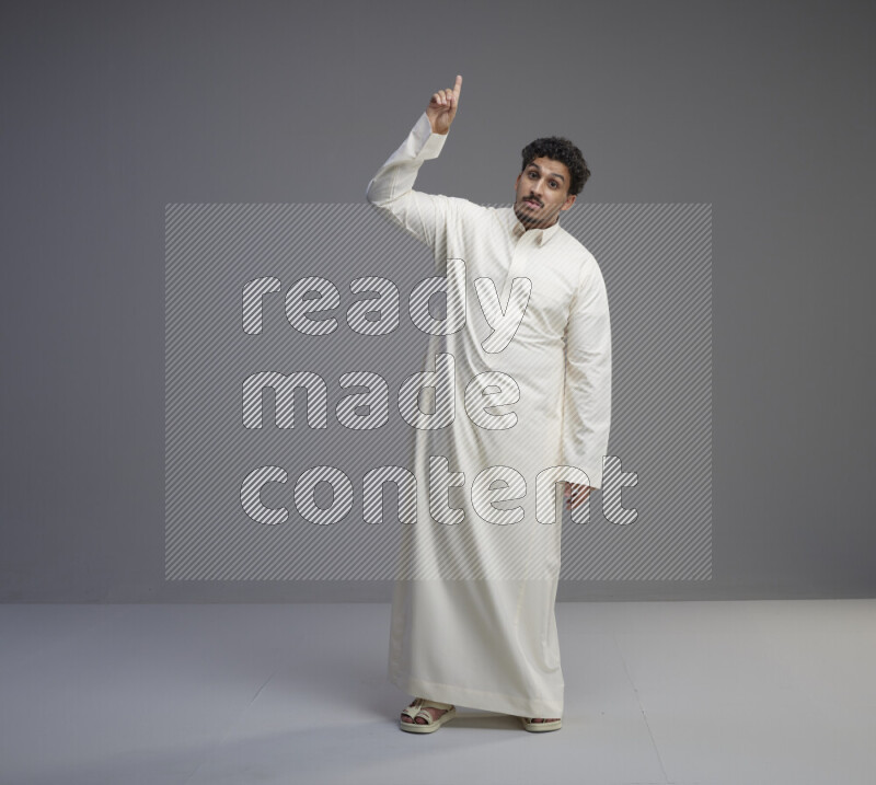 A Saudi man standing wearing thob interacting with the camera on gray background