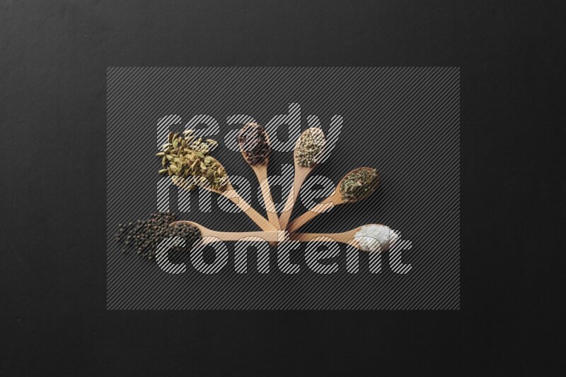 wooden spoons filled with white peppers, cloves, cardamom, salt, black peppers and basil on black flooring