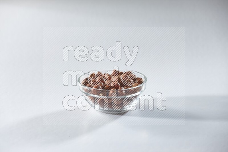 A glass bowl full of peeled hazelnuts on a white background in different angles