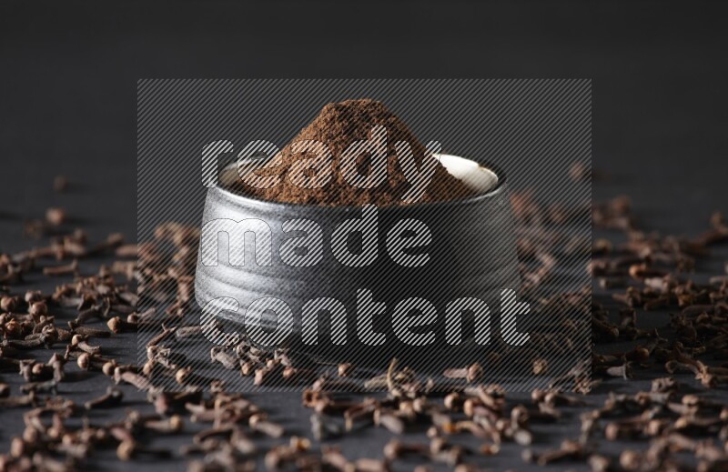 A black pottery bowl full of cloves powder and cloves whole grains on a black flooring
