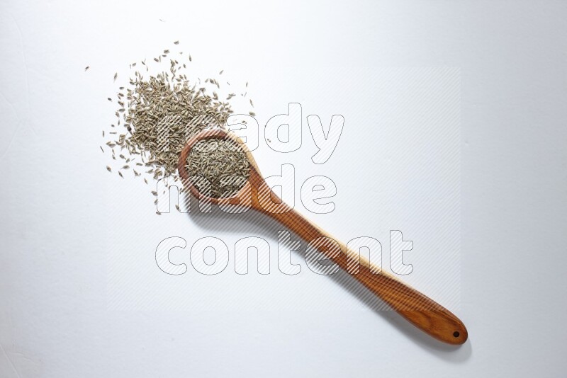 A wooden ladle full of cumin seeds on a white flooring