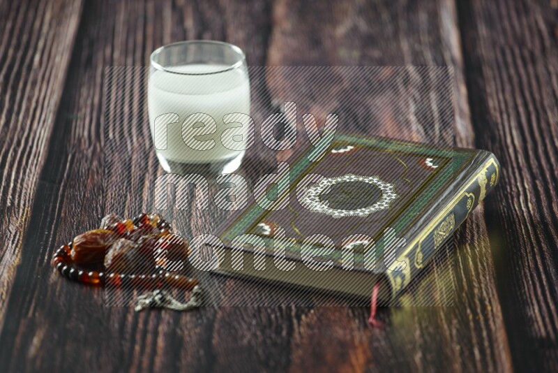 Quran with dates, prayer beads and different drinks all placed on wooden background