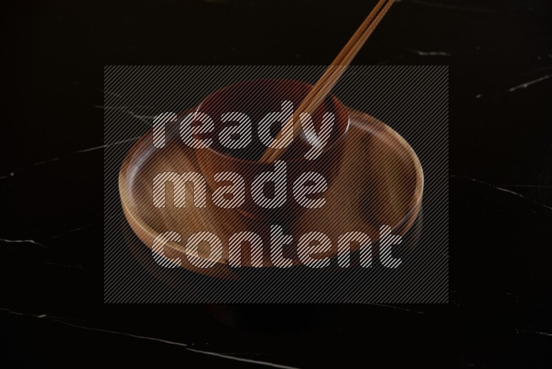 brown wood round bowl on top of brown wood round plate and wood chopsticks, on black marble countertop