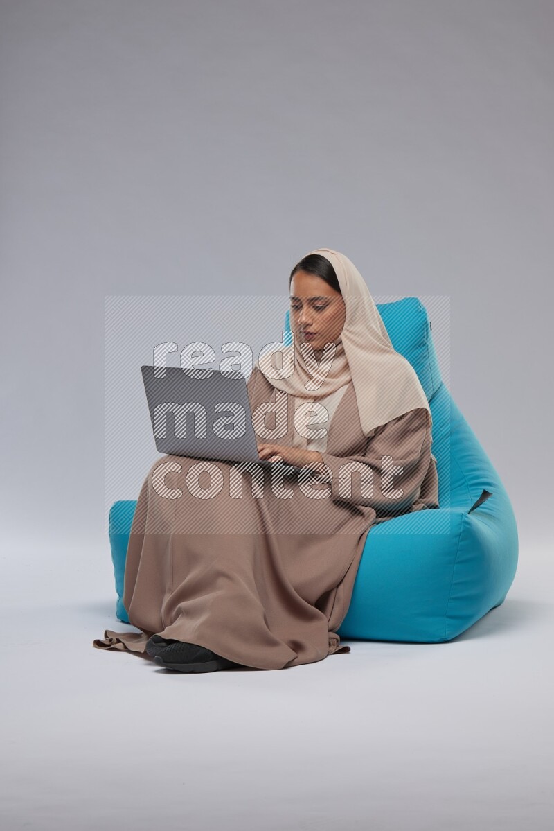 A Saudi woman sitting on a blue beanbag and working on laptop
