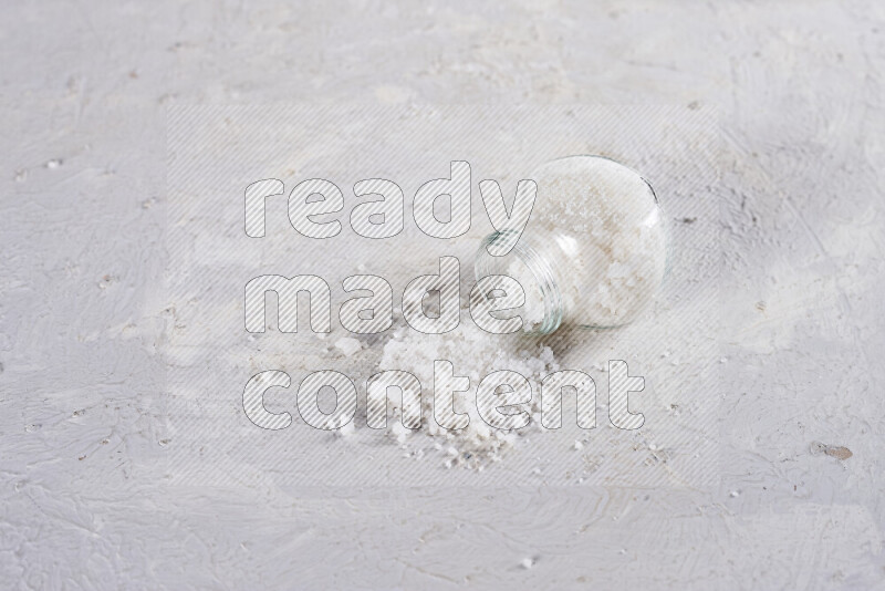 A glass jar full of coarse sea salt crystals on white background