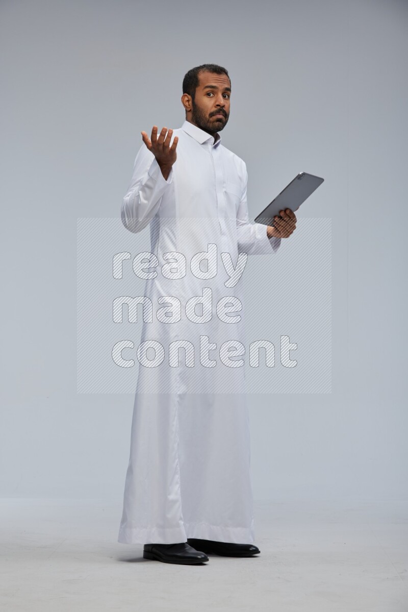 Saudi man wearing Thob standing working on tablet on Gray background
