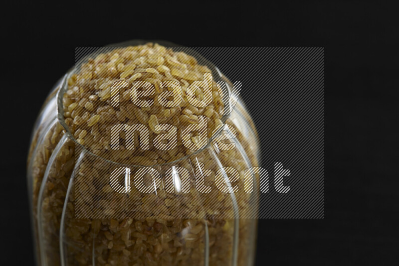 Coarse bulgur in a glass jar on black background