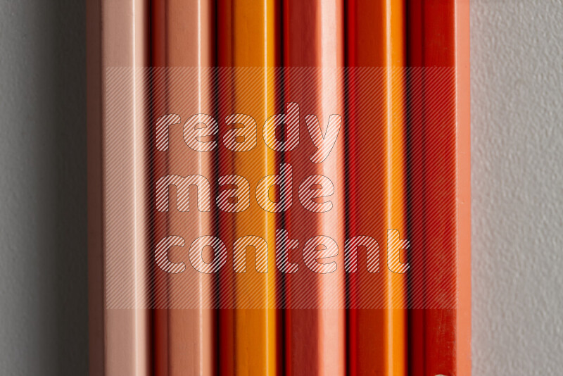 A collection of colored pencils arranged showcasing a gradient of orange hues on grey background