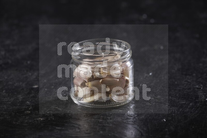 A glass jar full of garlic cloves on a textured black flooring in different angles