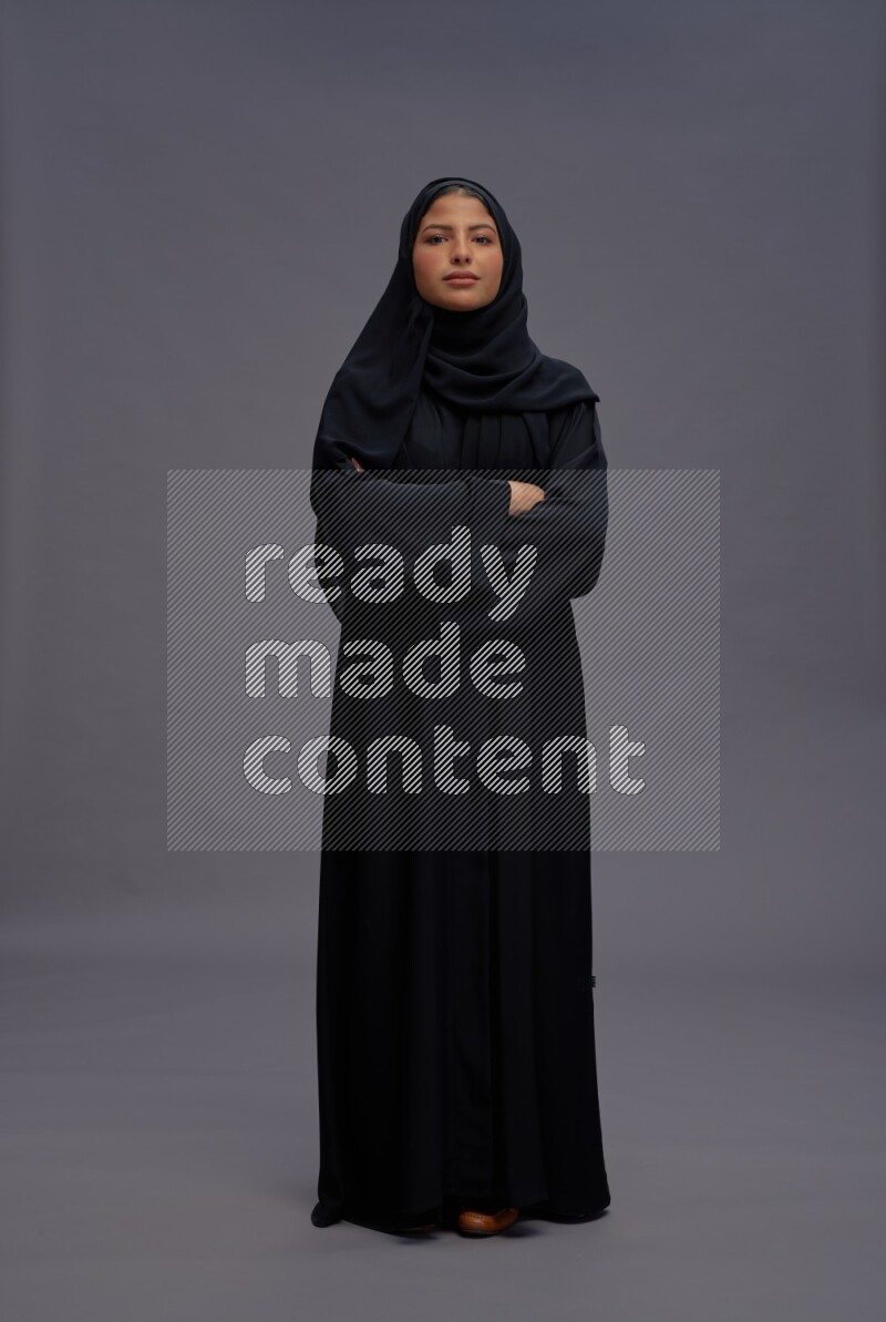 Saudi woman wearing Abaya standing with crossed arms on gray background