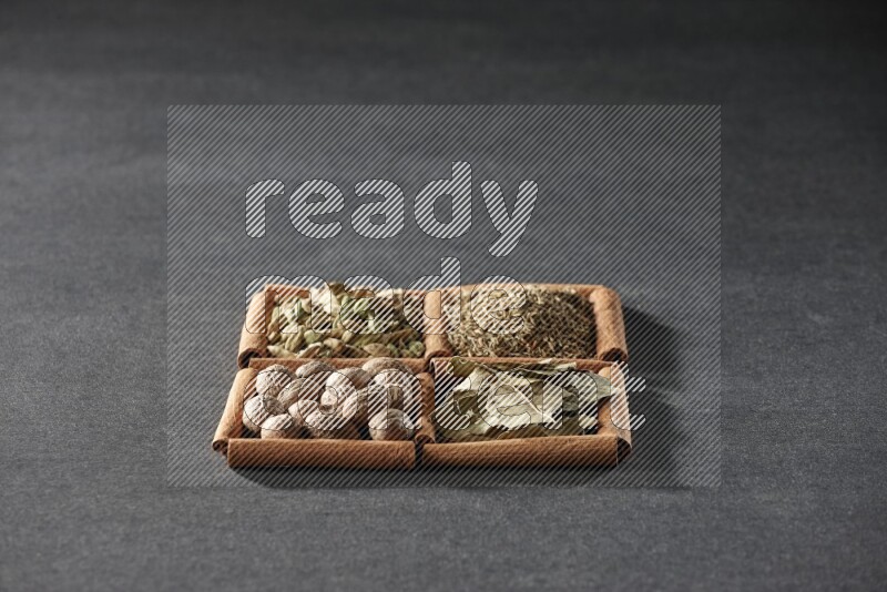 4 مربعات من عيدان القرفة ممتلئة بالكمون وحبوب الهيل وأوراق الغار وجوزة الطيب على أرضية سوداء