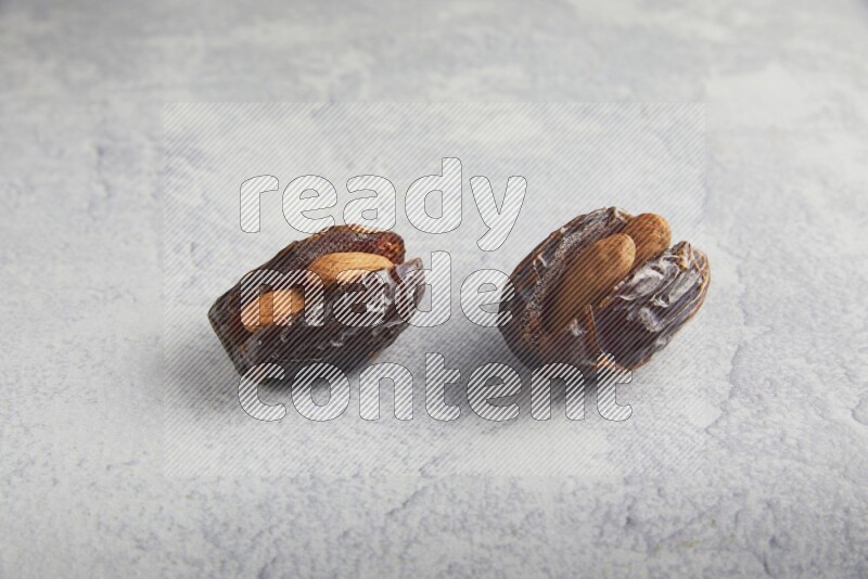 two almond stuffed madjoul dates on a light grey background