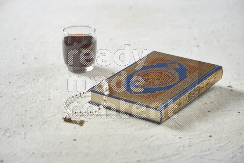 Quran with dates, prayer beads and different drinks all placed on textured white background