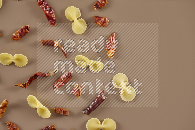 Raw pasta with different ingredients such as cherry tomatoes, garlic, onions, red chilis, black pepper, white pepper, bay laurel leaves, rosemary and cardamom on beige background
