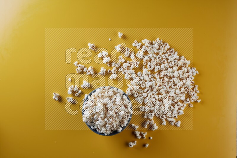 A blue pottery bowl full of popcorn with popcorn beside it on a yellow background in different angles