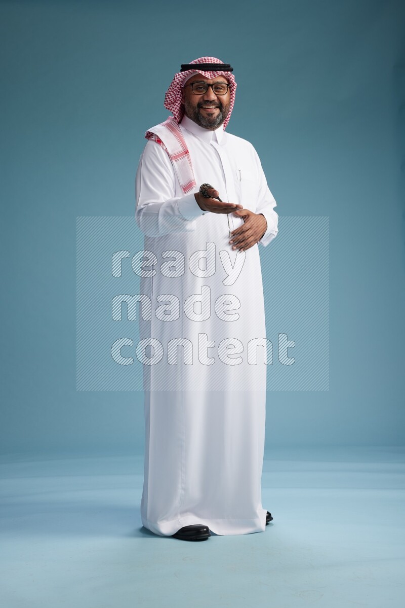 Saudi Man with shimag Standing Interacting with the camera on blue background