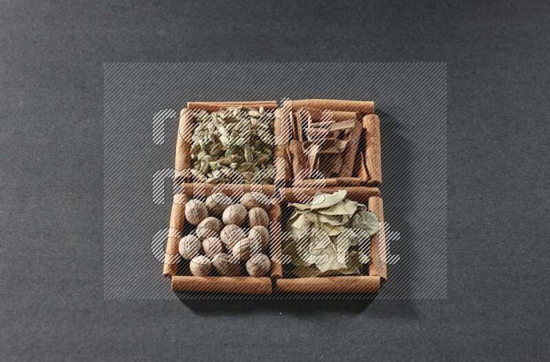 4 squares of cinnamon sticks full of cinnamon, cardamom, bay laurel leaves and nutmegs on black flooring