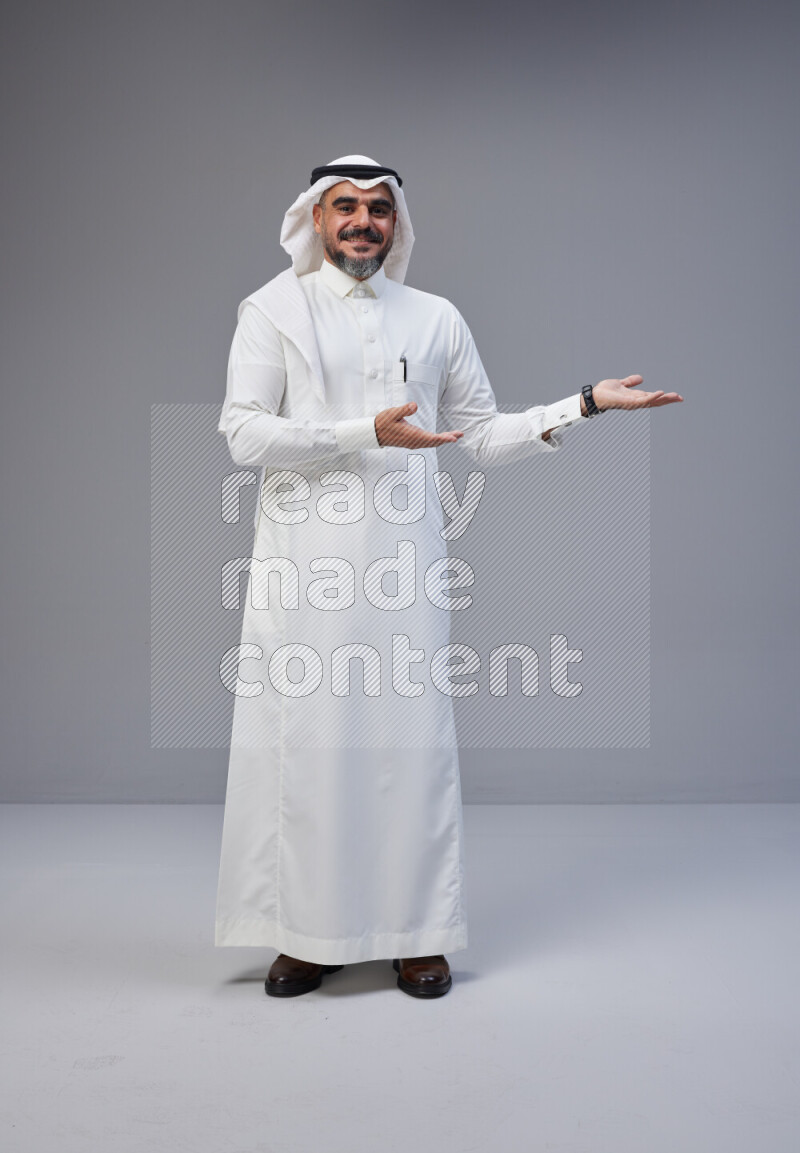 Saudi man Wearing Thob and white Shomag standing interacting with the camera on Gray background