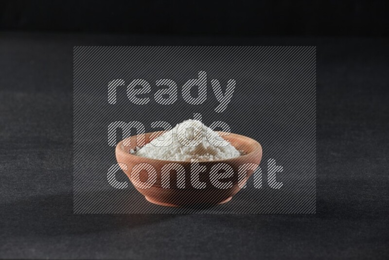 A wooden bowl full of desiccated coconut on a black background in different angles