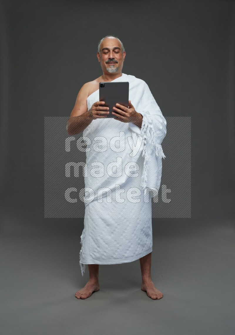 A man wearing Ehram Standing working on tablet on gray background