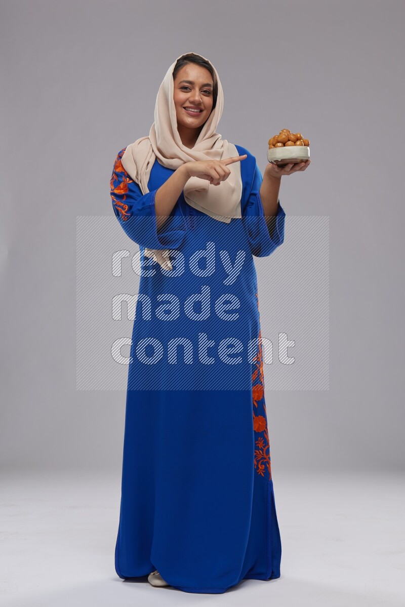 A Saudi woman standing wearing Jalabeya holding a plate of luqaimat