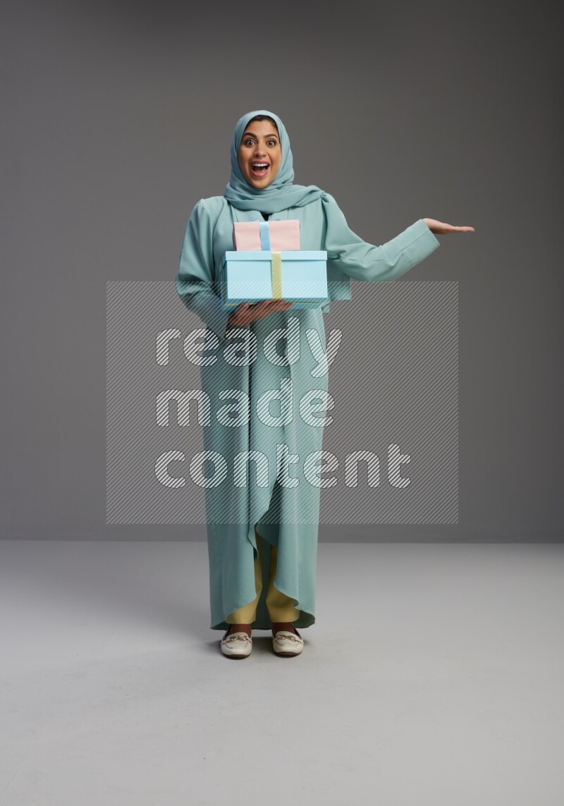 Saudi Woman wearing Abaya standing holding gift box on Gray background