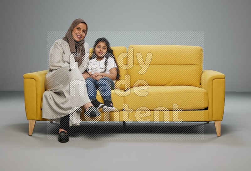 A girl with her mother sitting and interacting with the camera on gray background