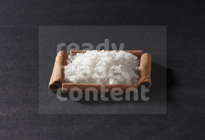 أربعة من أعواد القرفة مكونة شكل مربع بداخلها ملح أبيض علي خلفية سوداء