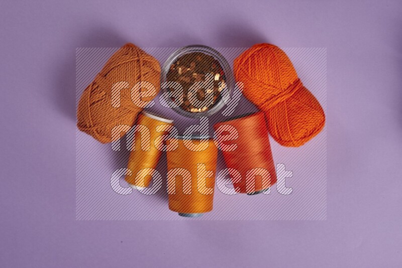 An orange collection of sewing and tailoring tools arranged on a purple background