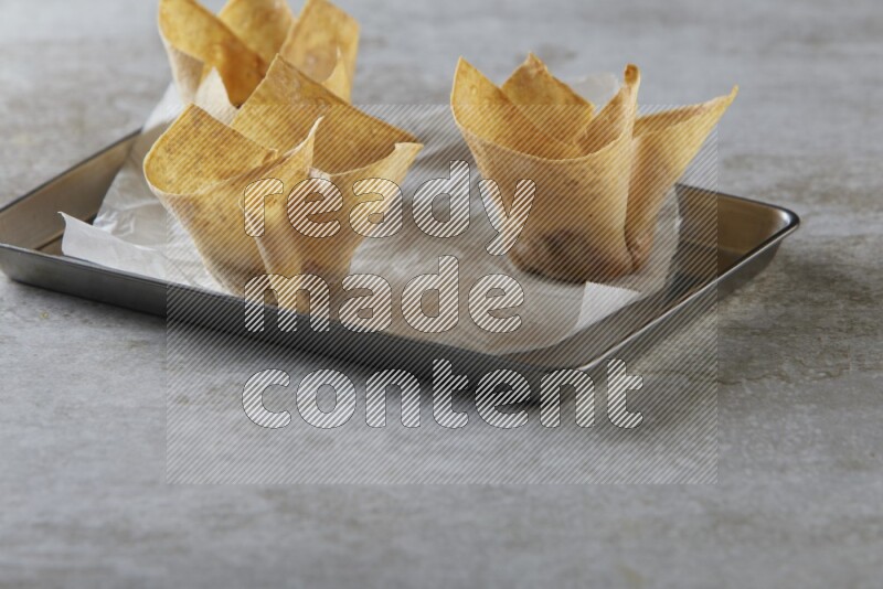 wonton cups on parchment paper in stainless tray on grey textured counter top