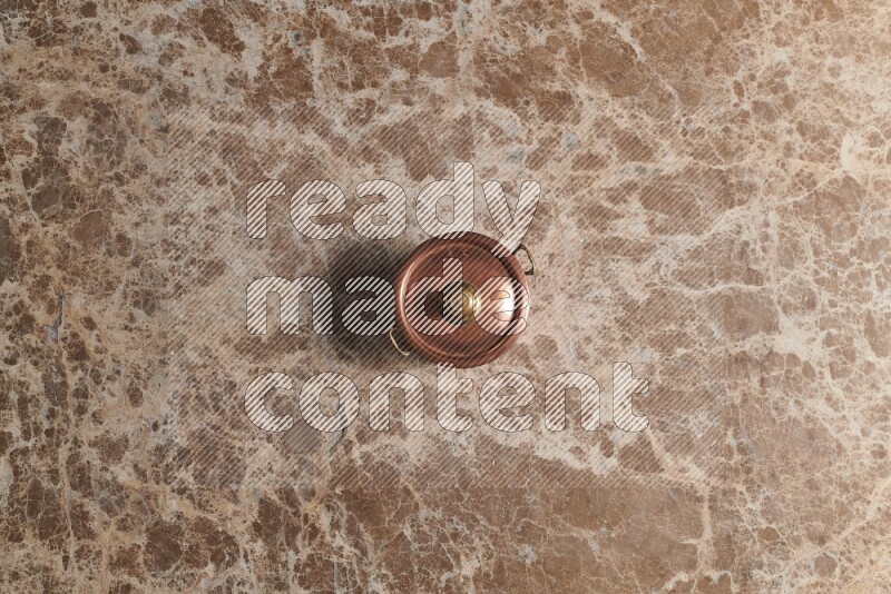 A small copper pot on beige marble background