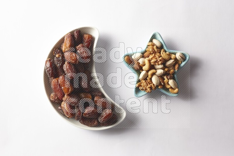 Dates in a crescent pottery plate and a star shaped plate with mixed nuts on white background